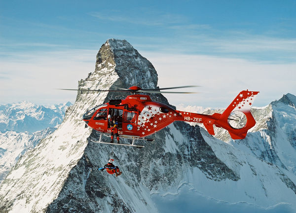 Air Zermatt helicopter with mountain rescuer on the longline; in the background, the Matterhorn.
